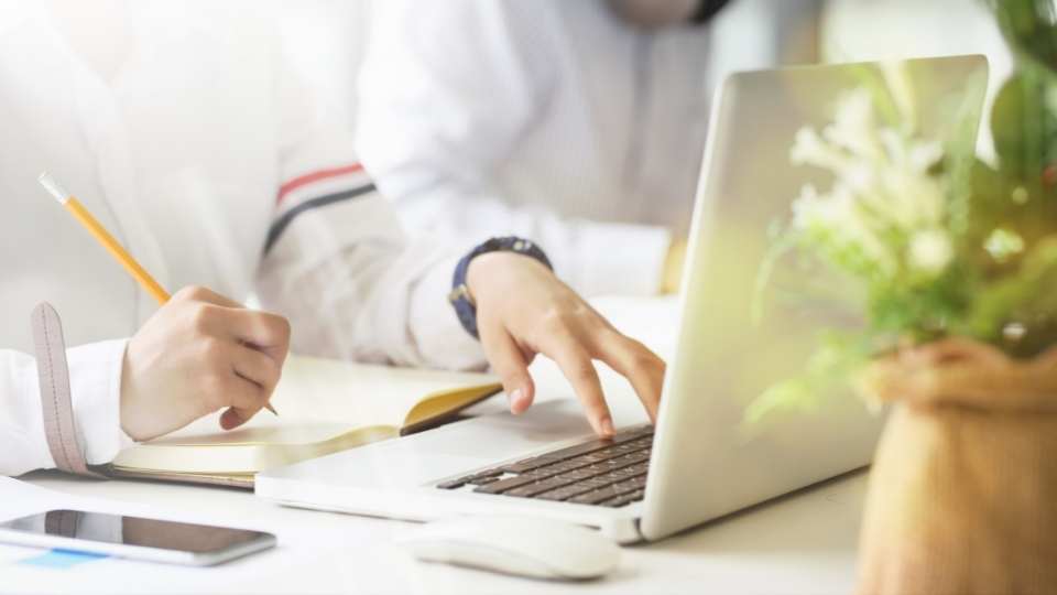 Zwei Personen sitzen um einen Laptop und tippen etwas