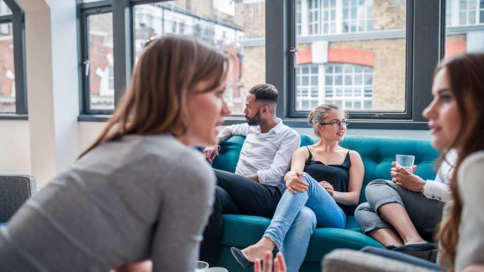 Frau spricht mit anderen Teammitgliedern auf einem Sofa